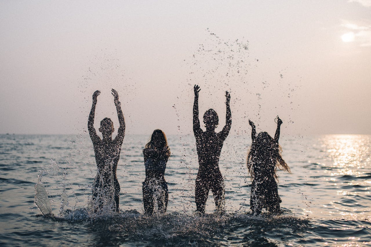 Minust Silhouettes of four people joyfully splashing water in the sea during a beautiful sunset.